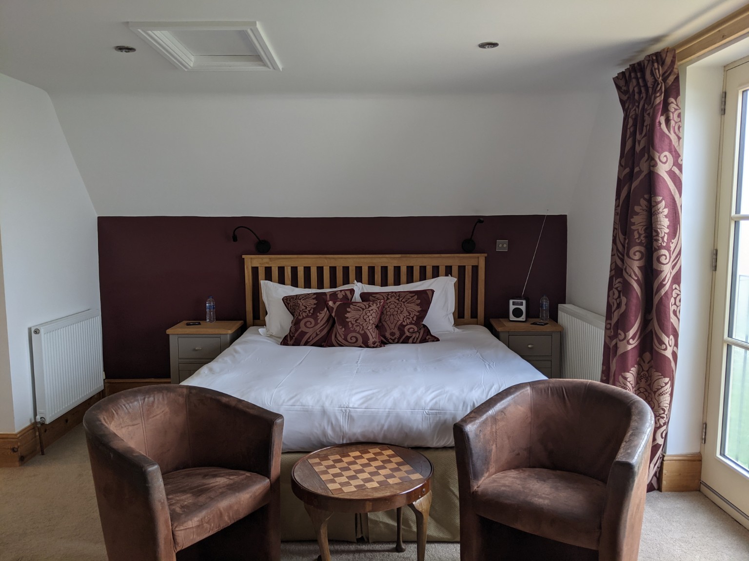 Robin: the king bed against the plum feature wall, with brown tub chairs by the glazed doors.